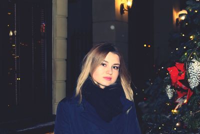 Portrait of young woman standing by christmas tree at home