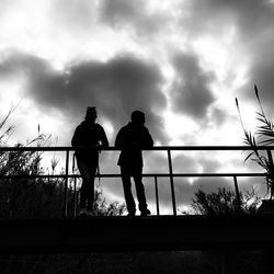 Silhouette people standing by railing against sky