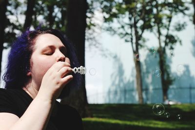 Young woman blowing bubbles against trees