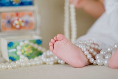 Low section of baby with pearl necklace at home