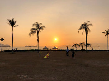 Silhouette palm trees on beach against sky during sunset