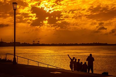 Silhouette people standing by sea against cloudy sky during sunset