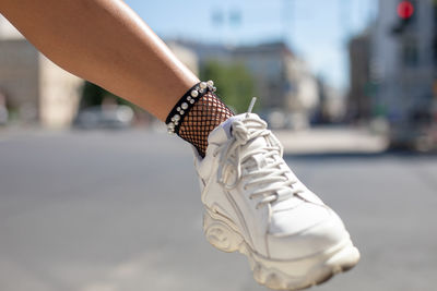 Low section of woman wearing white shoe on road in city during sunny day