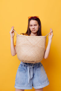 Portrait of smiling young woman standing against yellow background