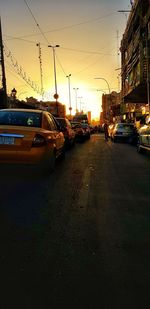 Cars on street by buildings against sky at sunset