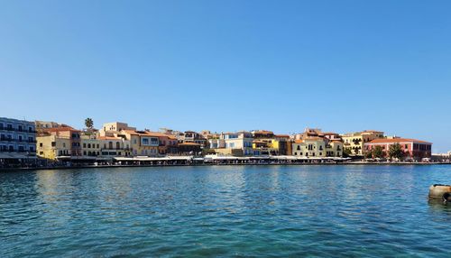 Buildings by river against clear blue sky