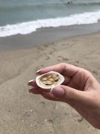 Midsection of person holding seashell with rings on beach
