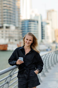 An attractive woman stands on the embankment and uses her phone while walking around the city