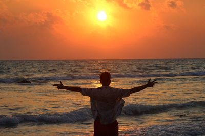 Rear view of man standing at beach during sunset