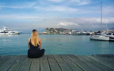 Rear view of woman sitting on pier looking at sea against sky