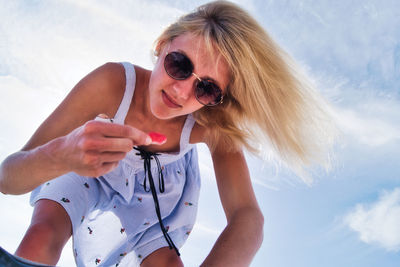 Low angle view of young woman wearing sunglasses while bending against sky