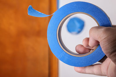 Close-up of hand holding adhesive tape against wall