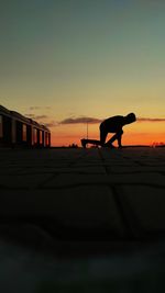 Rear view of man with dog on beach against sky during sunset