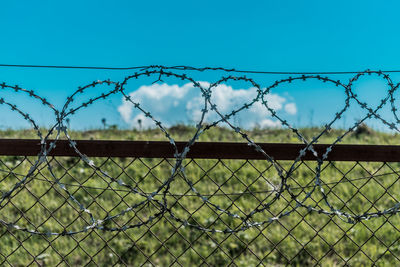 Barbed wire fence on field against sky