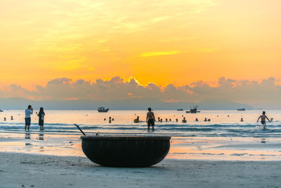 People on beach against sky during sunset