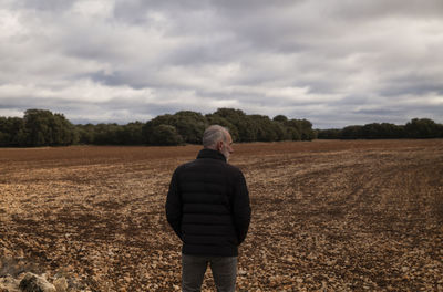 Adult man in winter clothes in fields against cloudy sky