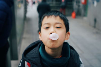 Close-up portrait of cute boy blowing bubble while standing on road