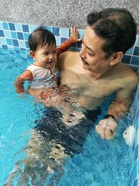 High angle view of shirtless man with daughter in swimming pool