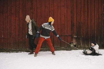 Mature woman pulling daughter on toboggan by girlfriend against cottage