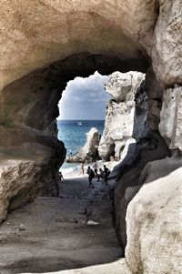 People on rock formation at sea shore against sky