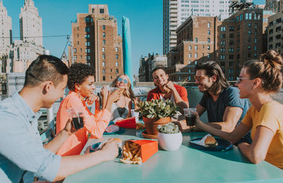 Happy friends enjoying snacks while talking on terrace