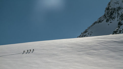 Silhouette people skiing on sow covered landscape against clear blue sky during sunny day
