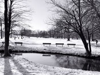 Bare trees by river against sky during winter