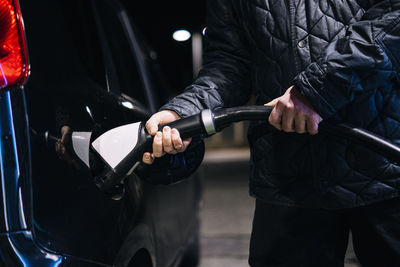 Man wearing jacket charging electric car at night