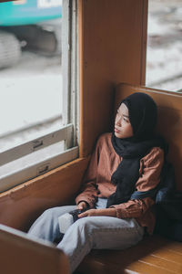 Young woman wearing hijab while sitting in train