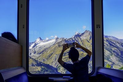 Rear view of man photographing mountains through smart phone in train