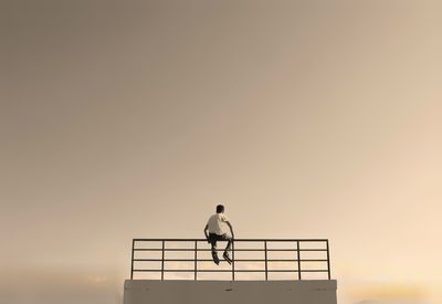 Silhouette kid standing on railing against sky