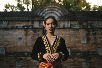 Portrait of young woman in traditional clothing standing against building