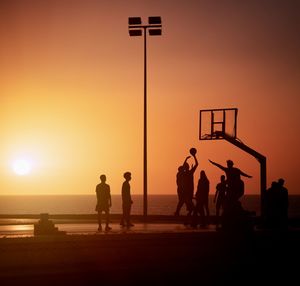 Silhouette people on playground playing basketball against sky during sunset