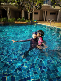 Mother and her adorable little daughter hugging each other in a swimming pool at a tropical resort