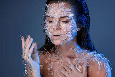 Close-up of woman with broken glass on body looking away against purple background