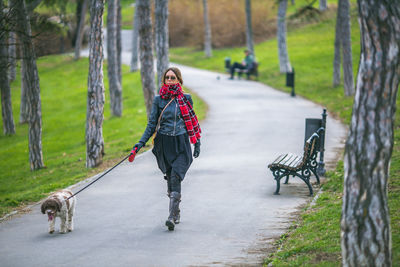 Full length of young woman with dog walking on footpath in park