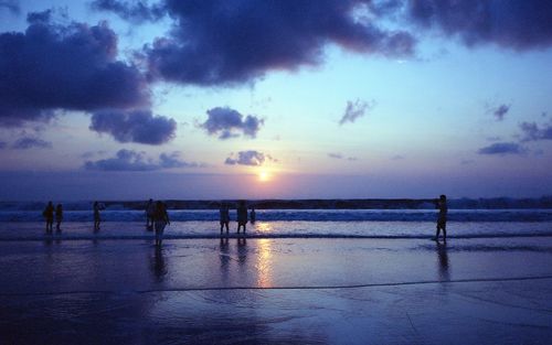 Silhouette people on beach against sky during sunset