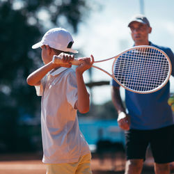 Coach teaching tennis to boy at court