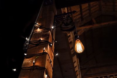 Low angle view of illuminated light bulb hanging by wooden column at night