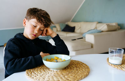 The boy sits over the plate and does not want to have a breakfast. no appetite.