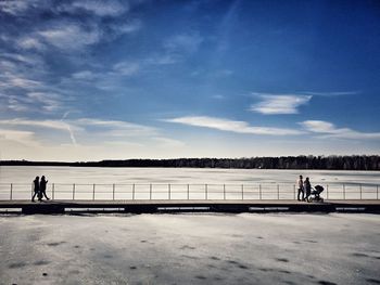 People walking on pier over frozen lake during winter
