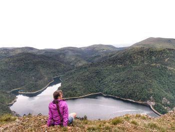 Rear view of woman sitting on mountain against clear sky