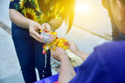 Midsection of woman pouring water on flowers held by friend during wedding ceremony