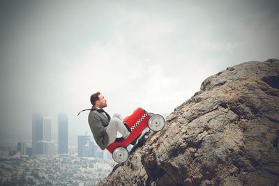 Side view of young man standing on rock against sky