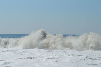 Waves splashing on shore against clear sky