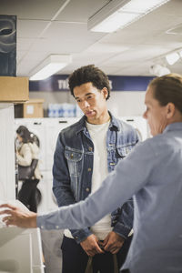 Mature owner explaining about washing machine to male customer in electronics store