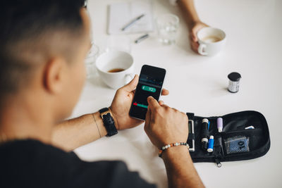 Businessman using mobile phone while doing blood sugar test at table during coffee break