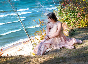 Young woman in a flowing dress sits high on a sandy cliff above lake michigan