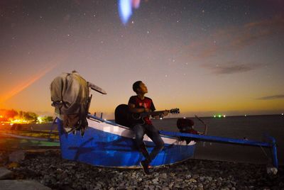 People sitting on beach by sea against sky at night
