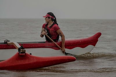 Man on red boat in sea against sky